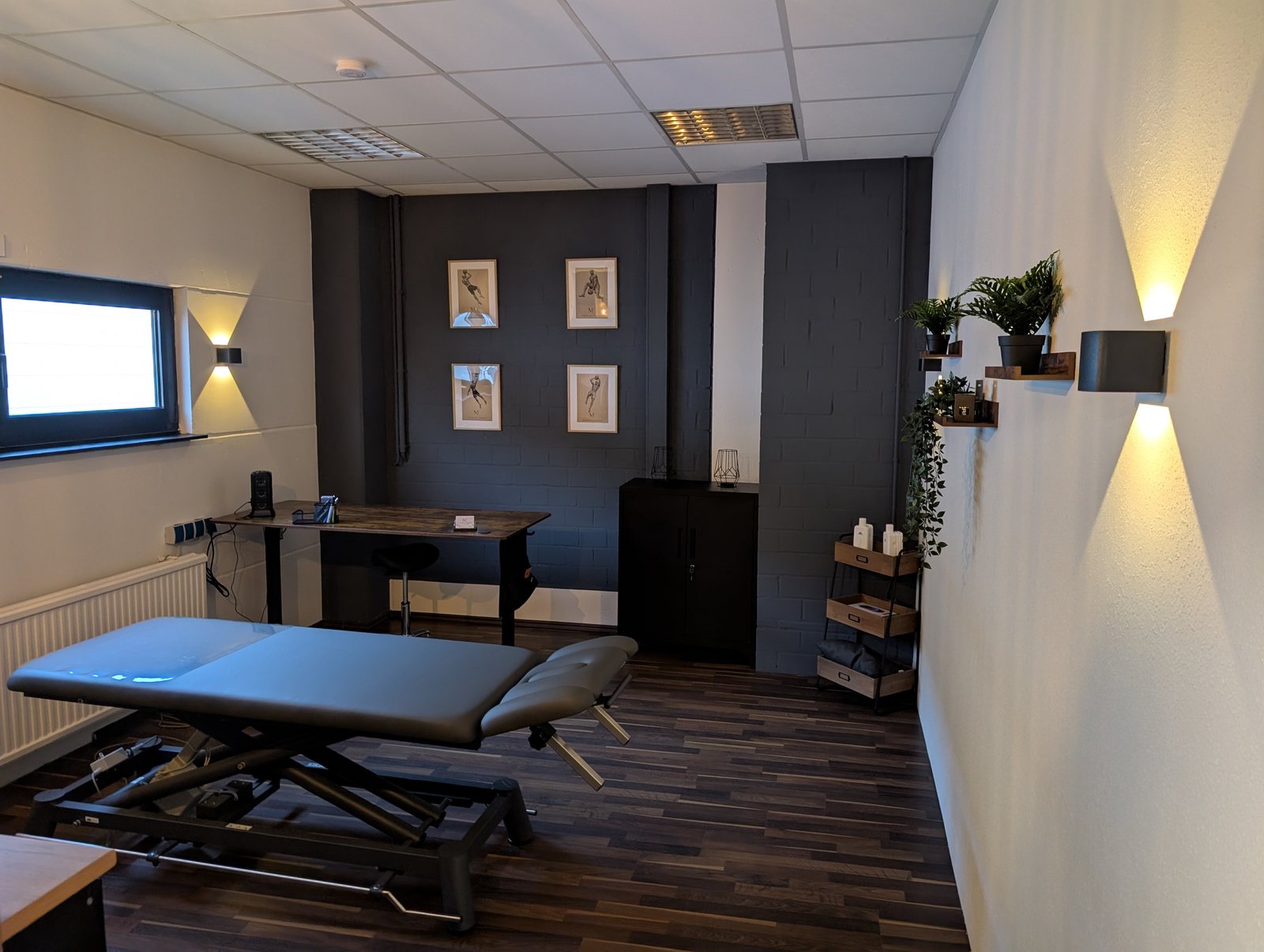 Behandlungsraum mit höhenverstellbarer Therapieliege, Schreibtisch und indirekter Beleuchtung