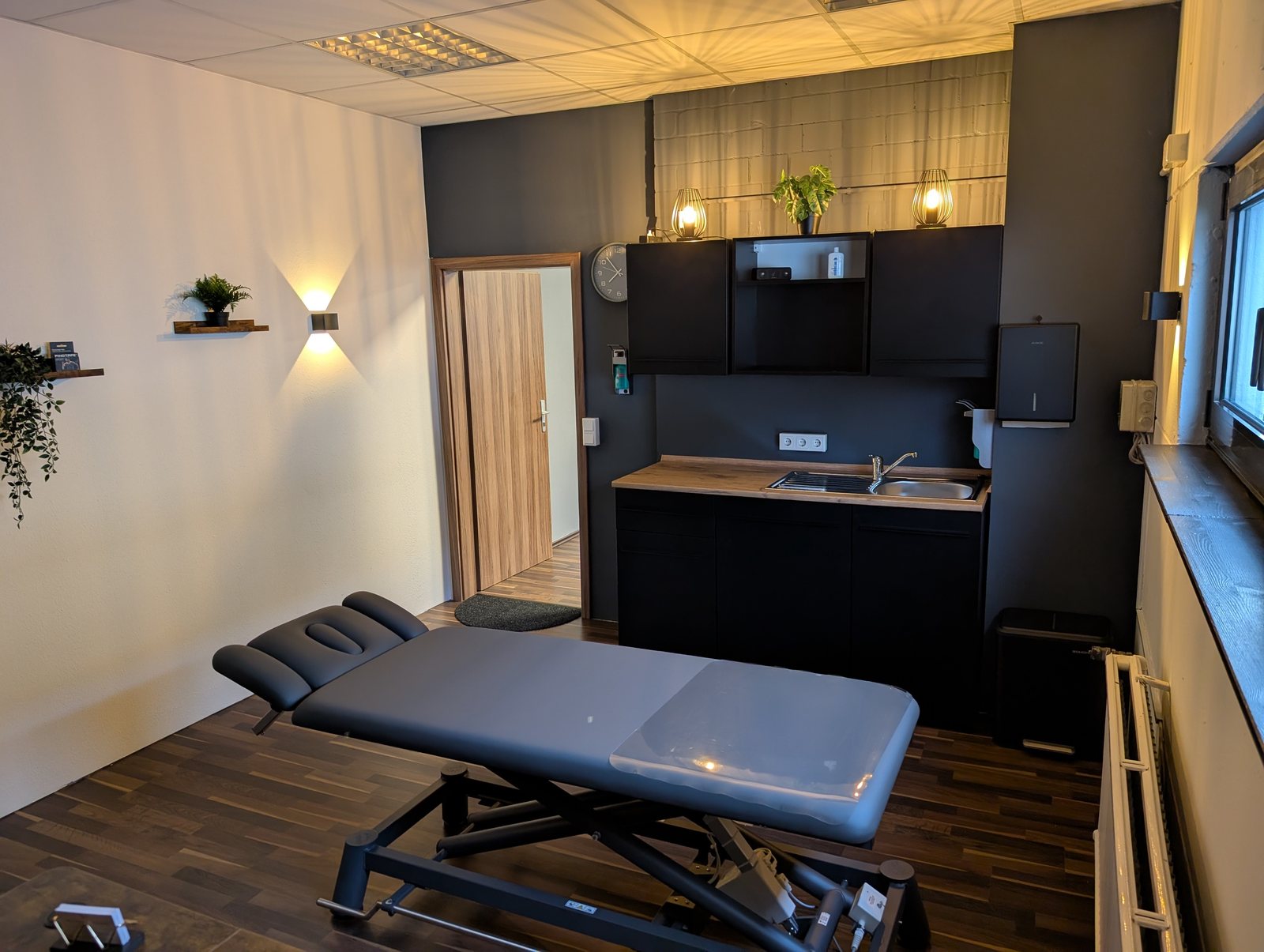 Blick auf Therapieliege, Waschbecken und Arbeitsbereich im Behandlungsraum